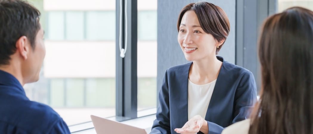 ビジネススーツ姿の女性が笑顔で二人の相手と会話している打ち合わせの様子